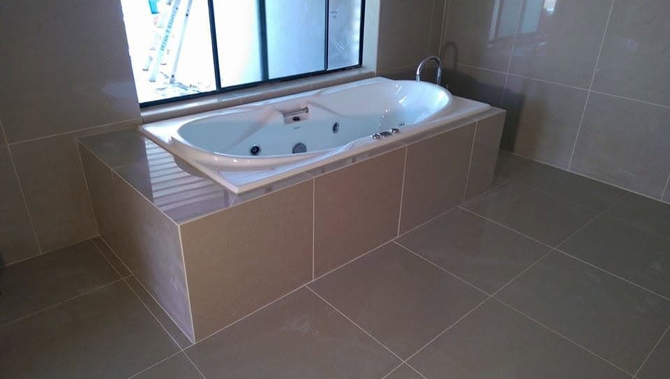 Freestanding bathtub on a large-format beige tile surround and matching floor tile