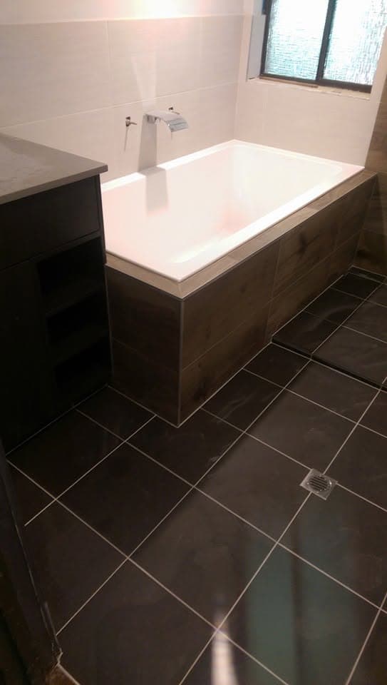 Bathroom with dark diagonally-laid floor tile and a timber-look tiled bath surround, white wall tile above