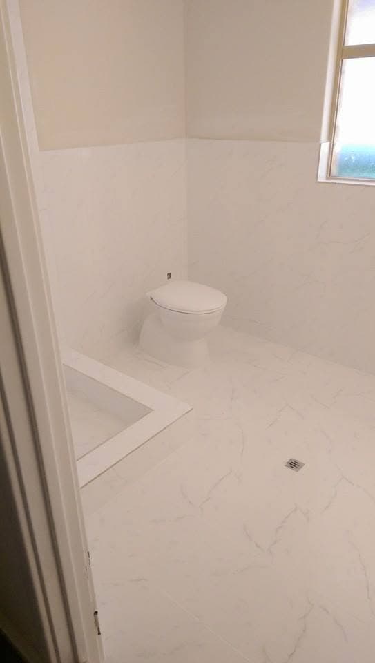 Bathroom with white marble-look floor tile and half-height wall tiling, toilet and bath step visible