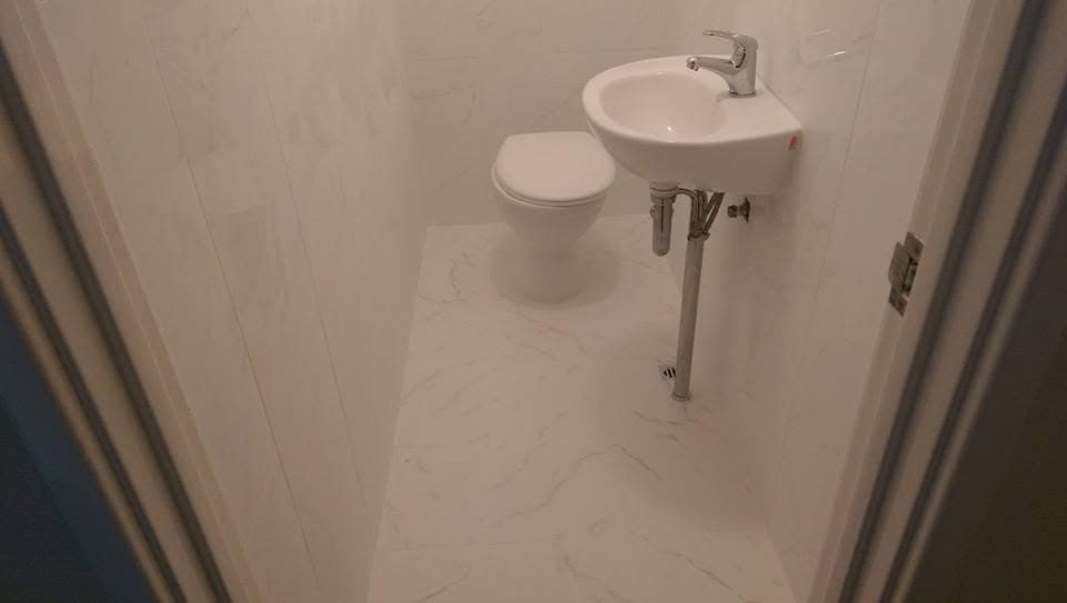 Small powder room fully tiled floor to ceiling in a white marble-look tile, with toilet and wall-hung basin
