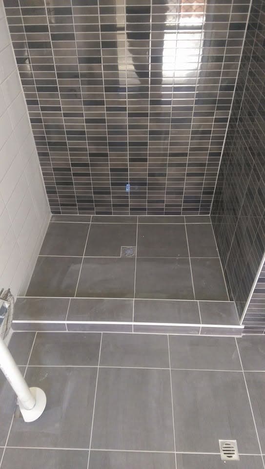 Shower recess lined with dark grey and charcoal mosaic tile, with a tiled hob step at the entry