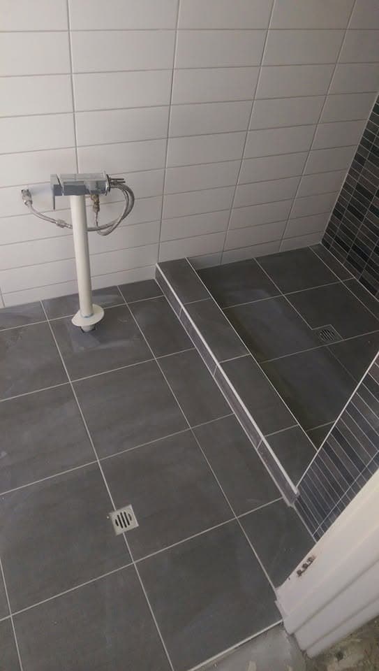Close-up of a tiled shower hob step and floor, with white subway tile walls