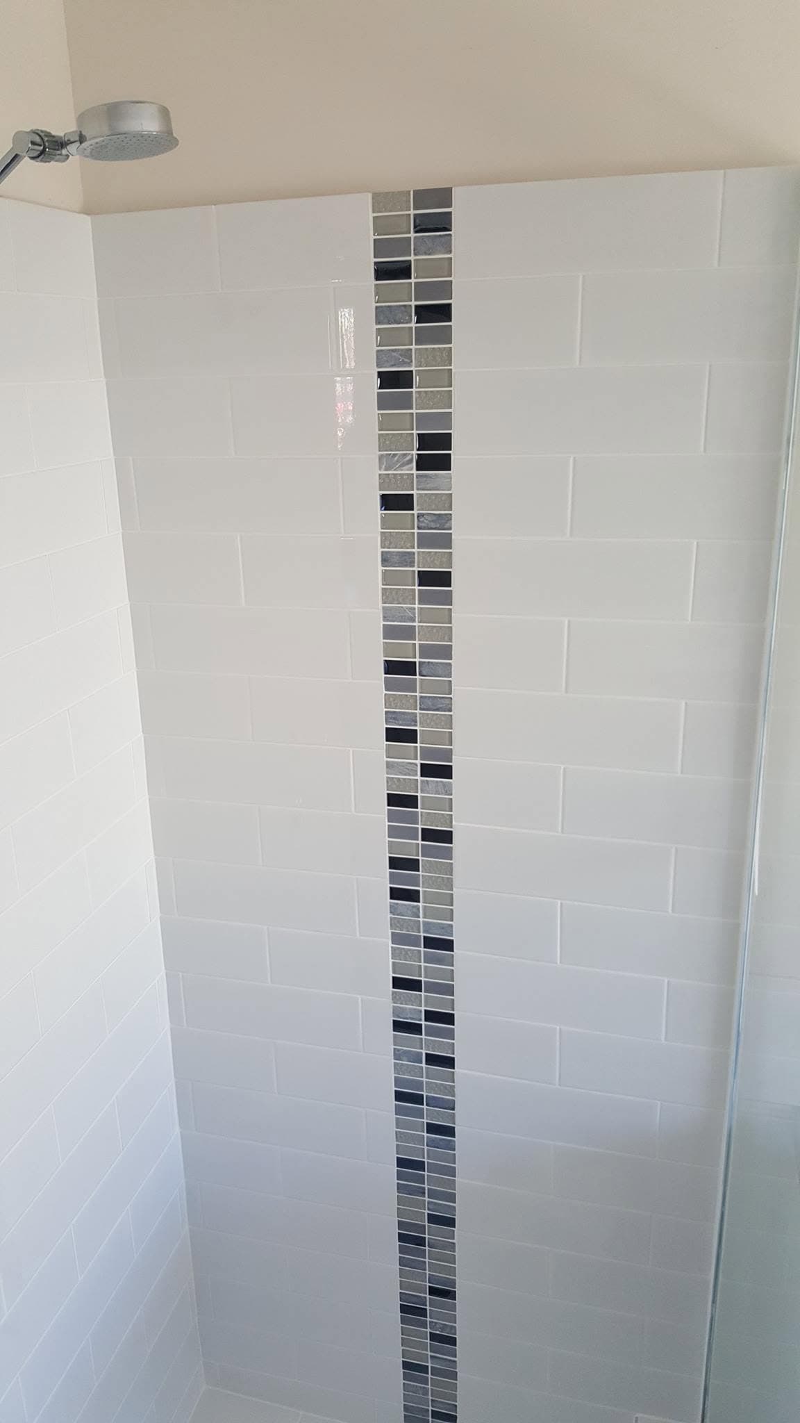 White subway tile shower wall with a vertical black, grey and white mosaic feature strip