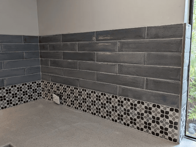 Grey brick-pattern feature wall tiling with a mosaic pattern border, next to a glass sliding door