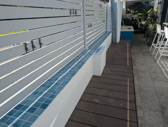 Blue mosaic tile capping the top edge of a low outdoor wall beside a timber deck