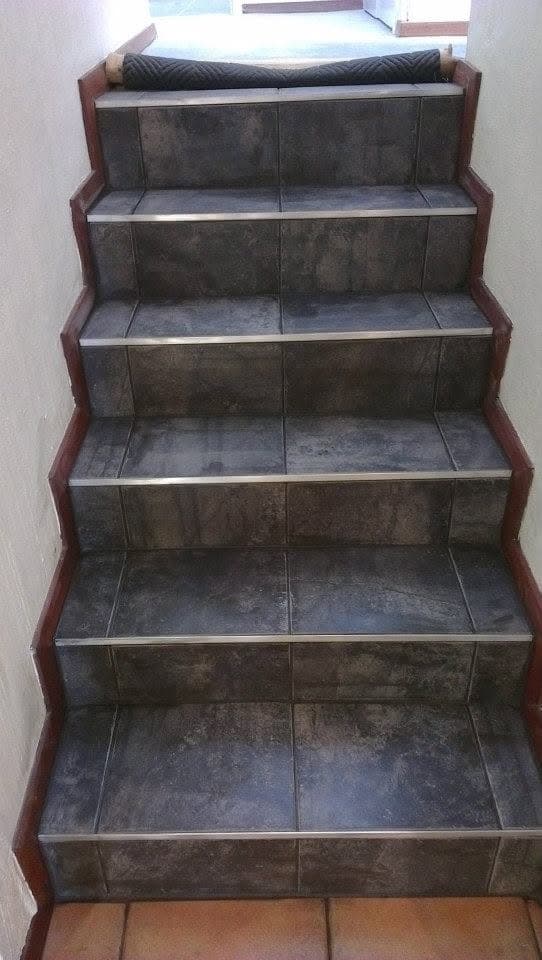 Staircase fully tiled in a dark stone-look tile, with metal stair-nosing trims and timber stringers