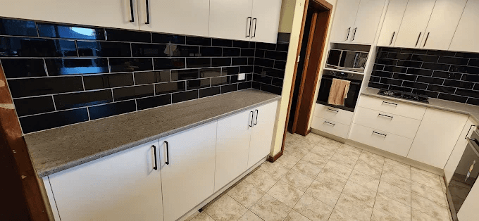 Black gloss subway tile kitchen splashback along a benchtop with white cabinetry
