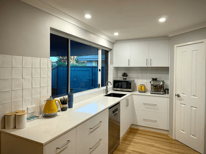 Kitchen with a white square tile splashback around a window above the sink