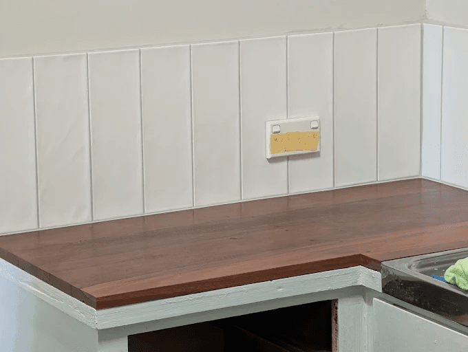 White vertical subway-style tile kitchen splashback above a timber benchtop, with a power point cut in