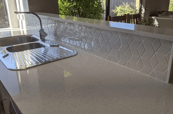 White three-dimensional geometric cube-pattern tile splashback behind a kitchen sink and tap